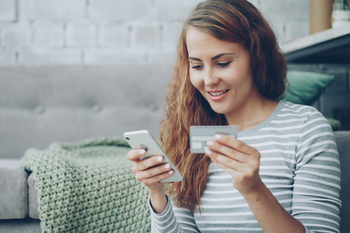 A woman shops online on her phone, bank card in hand.