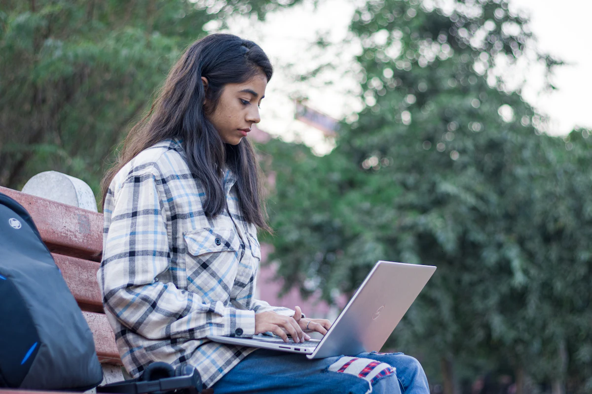 A student works on her laptop on a campus bench.