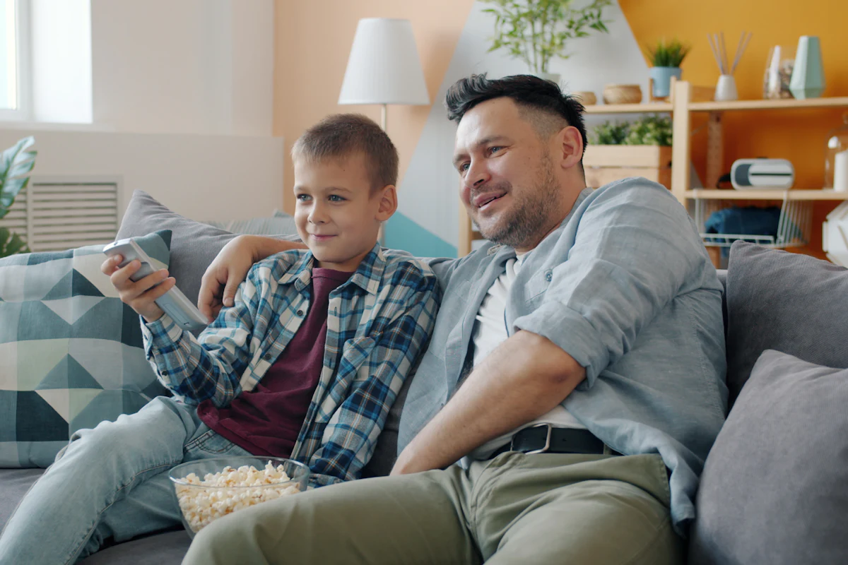 A father and son watch television together on the sofa.